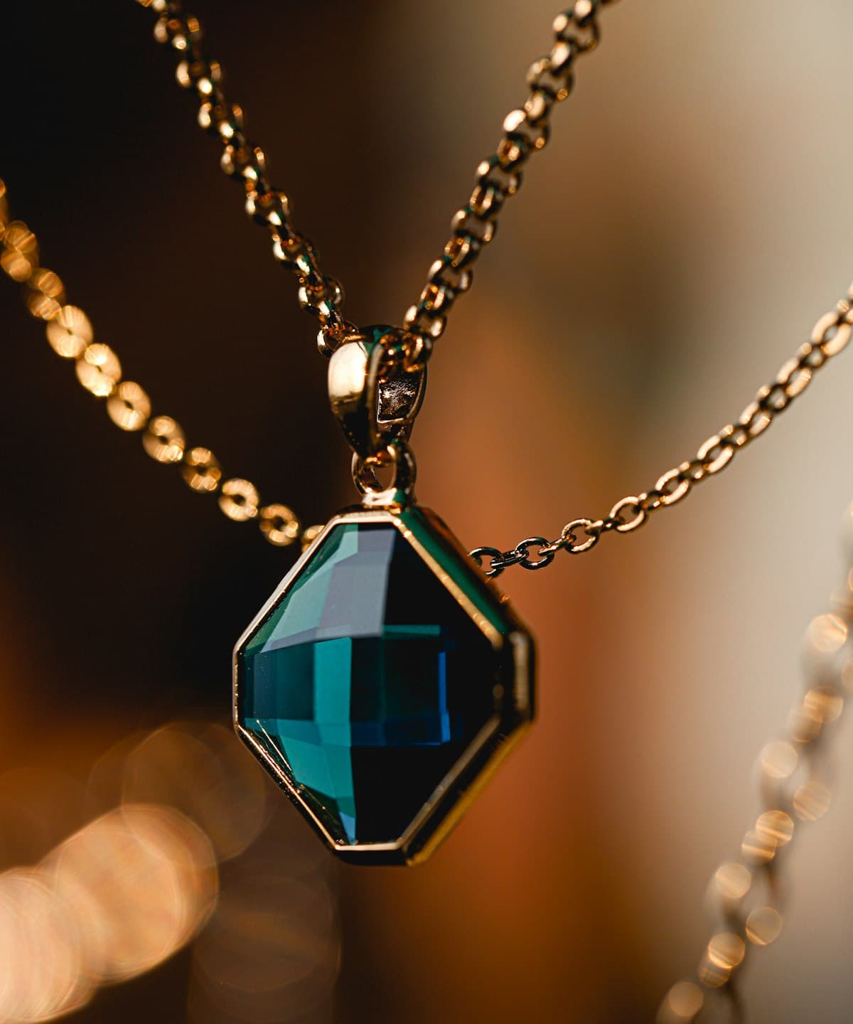 An emerald and diamond pendant on a fine chain, lit softly in a jewel box